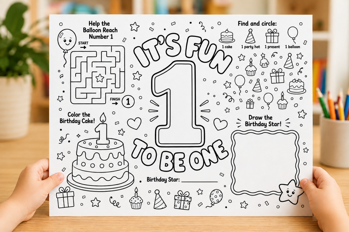 A child's first birthday coloring page held up by two hands on a wooden table. The page features black and white line art with activities like a balloon maze, coloring a birthday cake, and drawing a star, with the text 'IT'S FUN TO BE ONE'.
